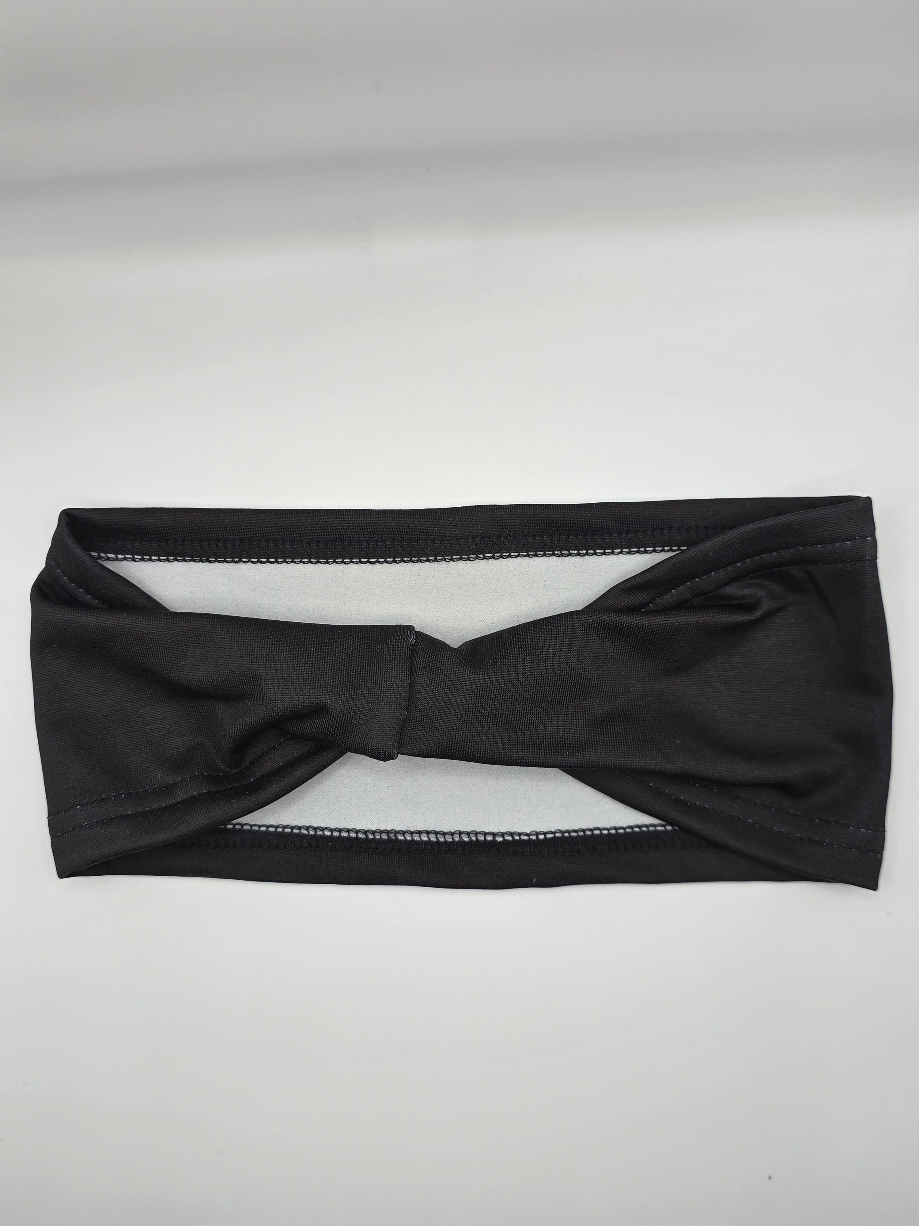 A black twisted knot headband laid flat on a light gray background.
