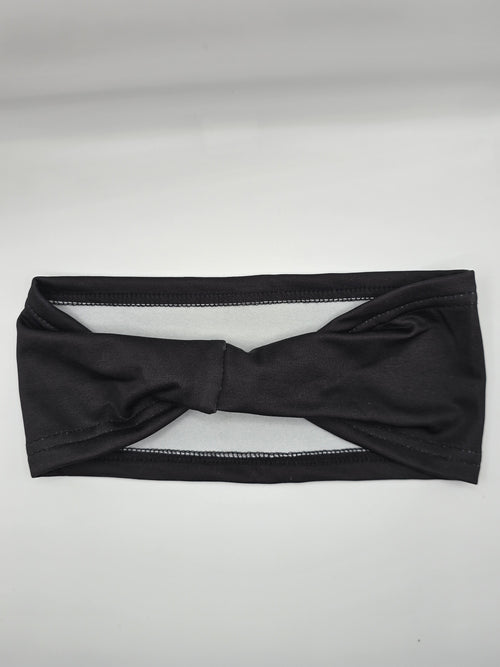 A black twisted knot headband laid flat on a light gray background.