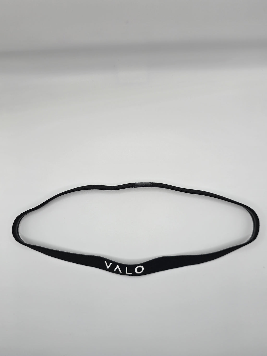 A black silicone headband with the brand name 'VALO' printed in white on the front, laid flat on a light gray background.
