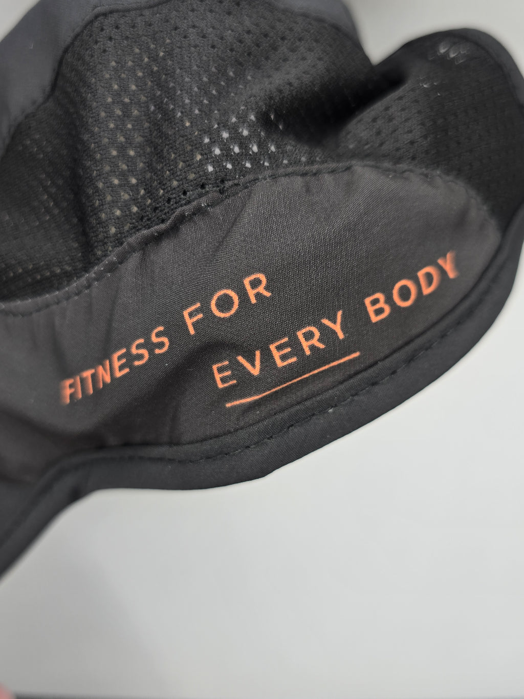Close-up of a black athletic glove with orange text reading 'FITNESS FOR EVERY BODY' on the palm side, showing a breathable mesh texture.