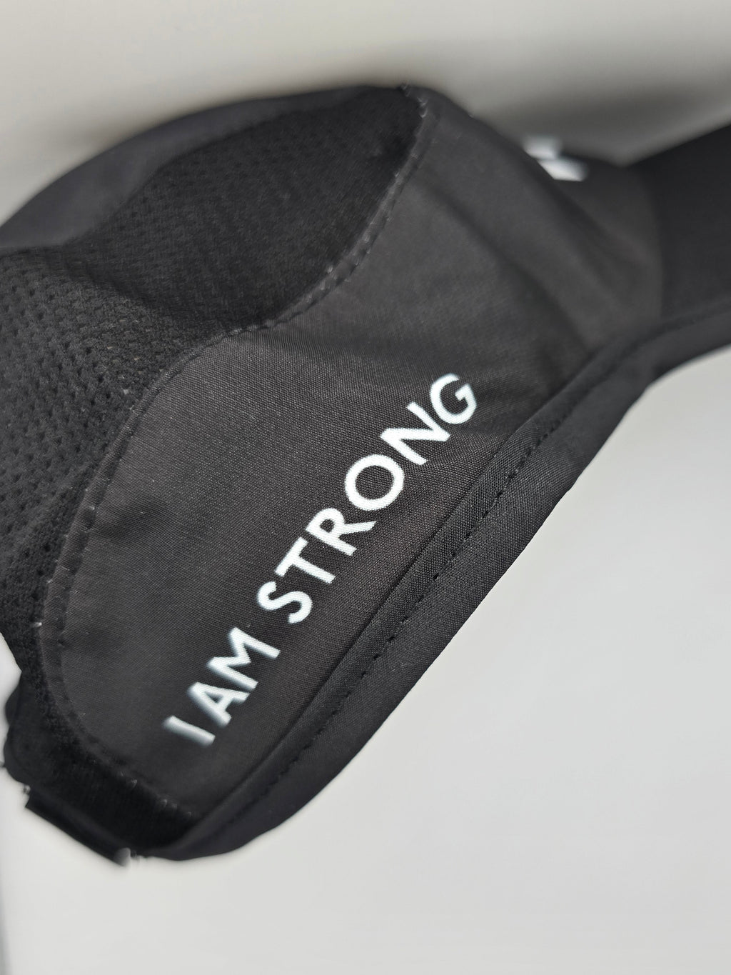 A close-up of a black athletic hat with the words 'I AM STRONG' printed in white capital letters on the side, set against a light gray background.