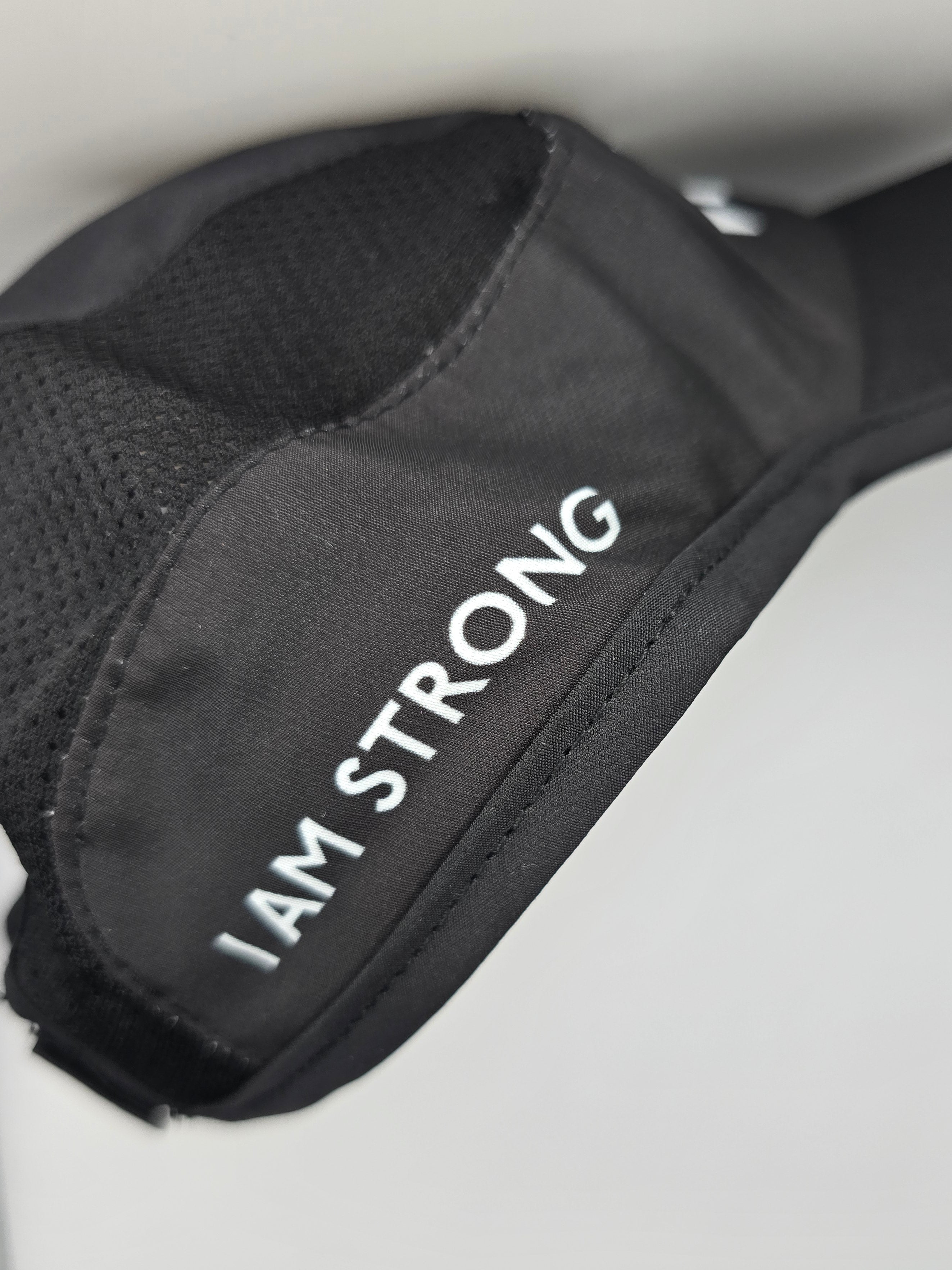 A close-up of a black athletic hat with the words 'I AM STRONG' printed in white capital letters on the side, set against a light gray background.