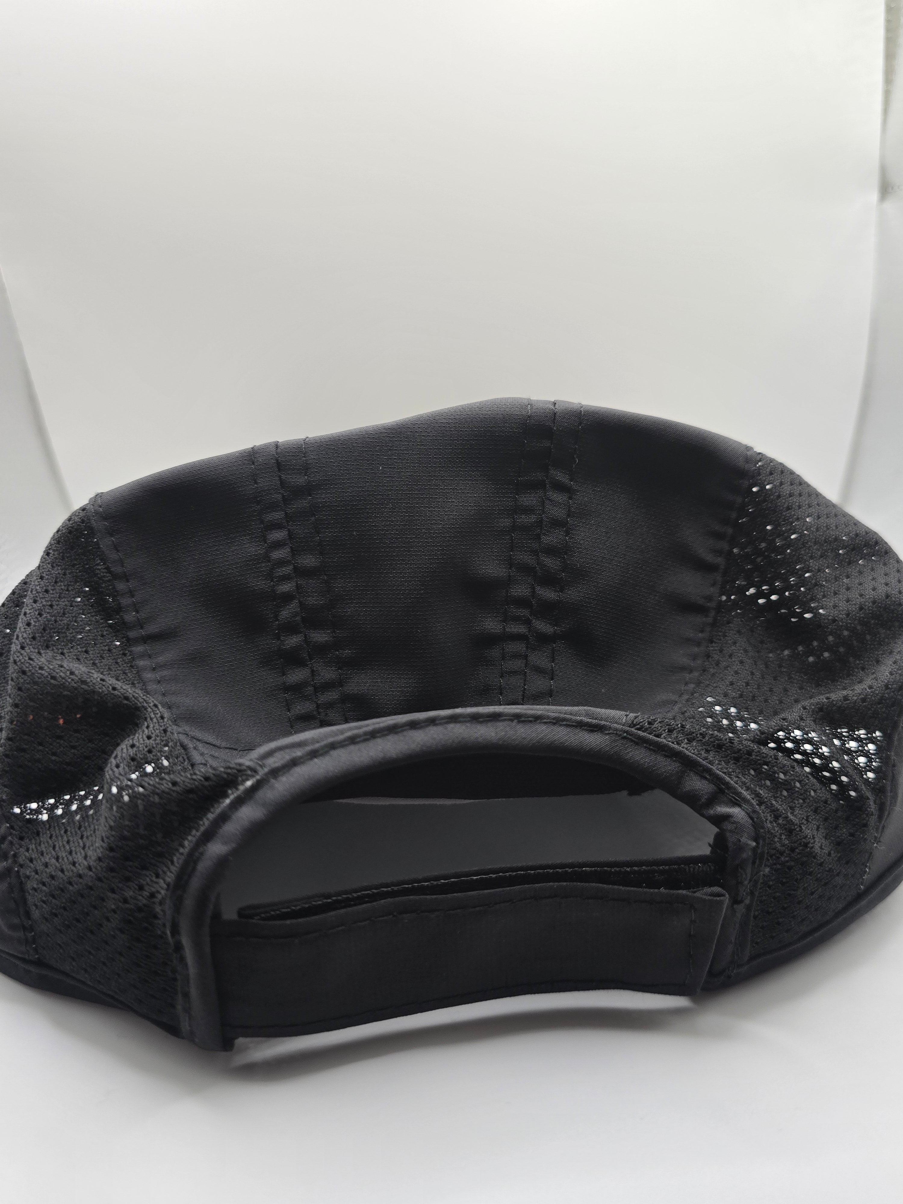 Black athletic cap with a breathable mesh back and adjustable hook-and-loop strap closure, photographed on a white background.